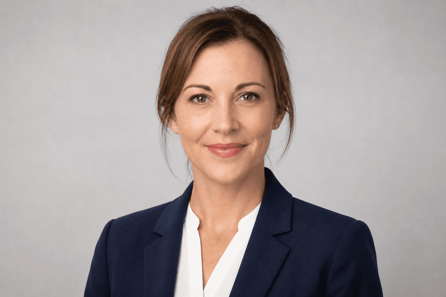 Classic LinkedIn profile picture — business headshot of a woman in a navy blazer and white blouse against a neutral light grey backdrop, direct eye contact, restrained smile