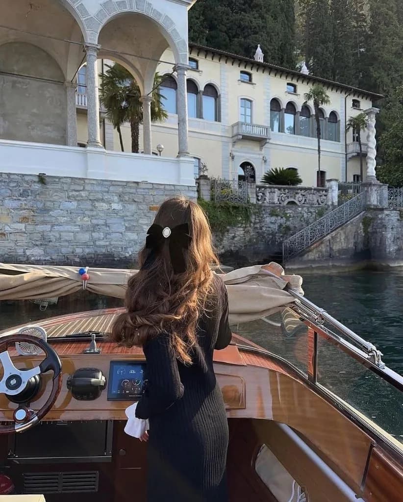 Junge Frau in schwarzem Kleid auf einem klassischen Holzboot vor einer Villa am Comer See